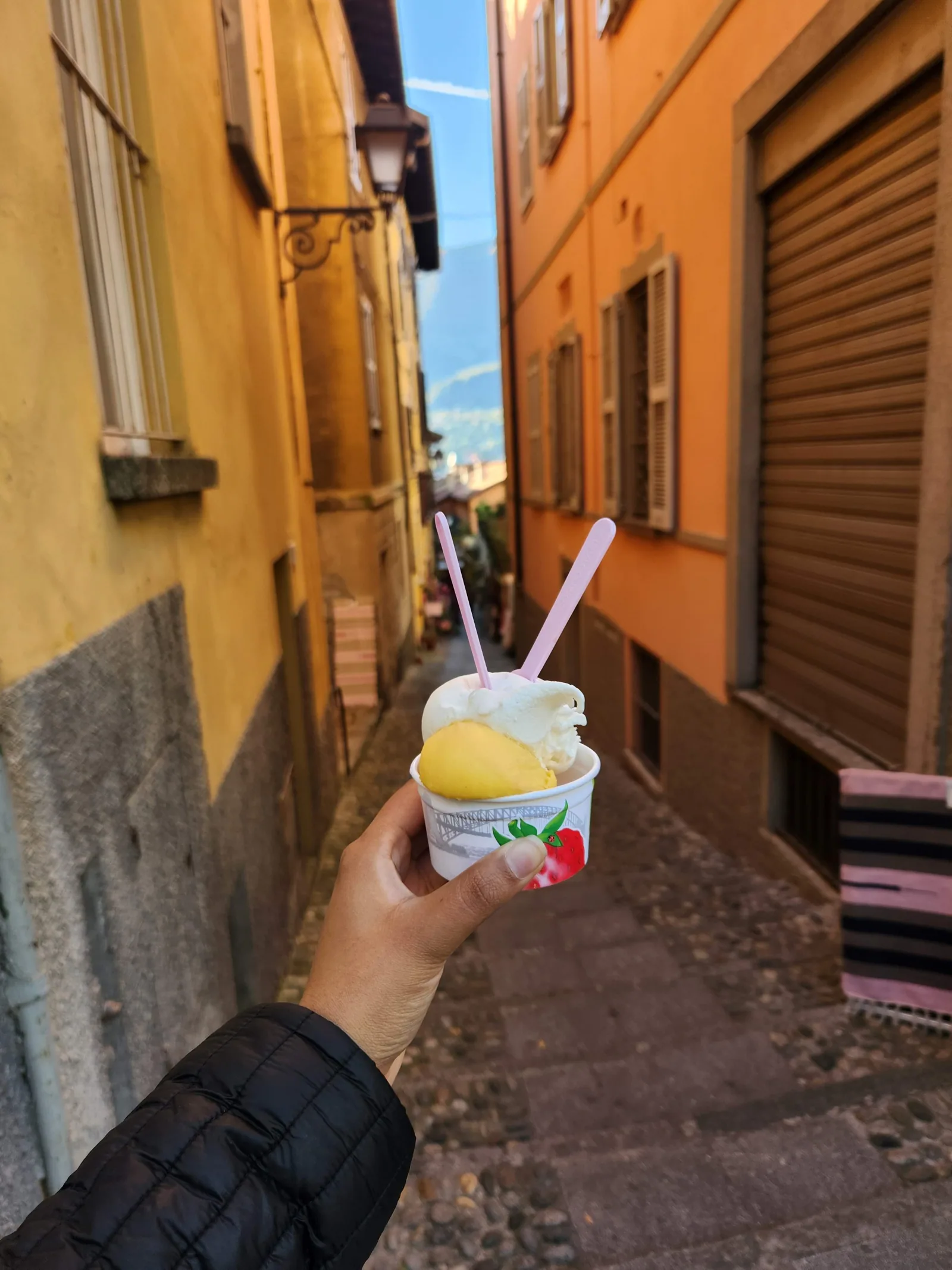 A cup of gelato held against an orange wall in a Lake Como village