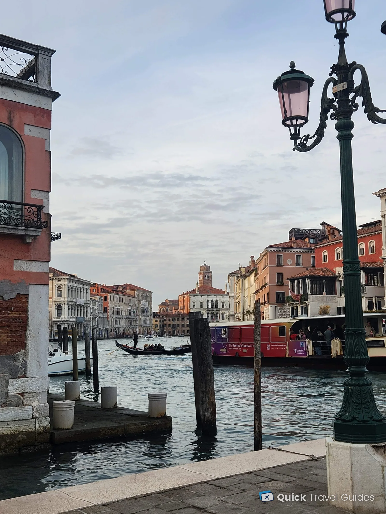 A gondola and a vaporetto on the Grand Canal, framed by a street lamp and a red palazzo, Venice
