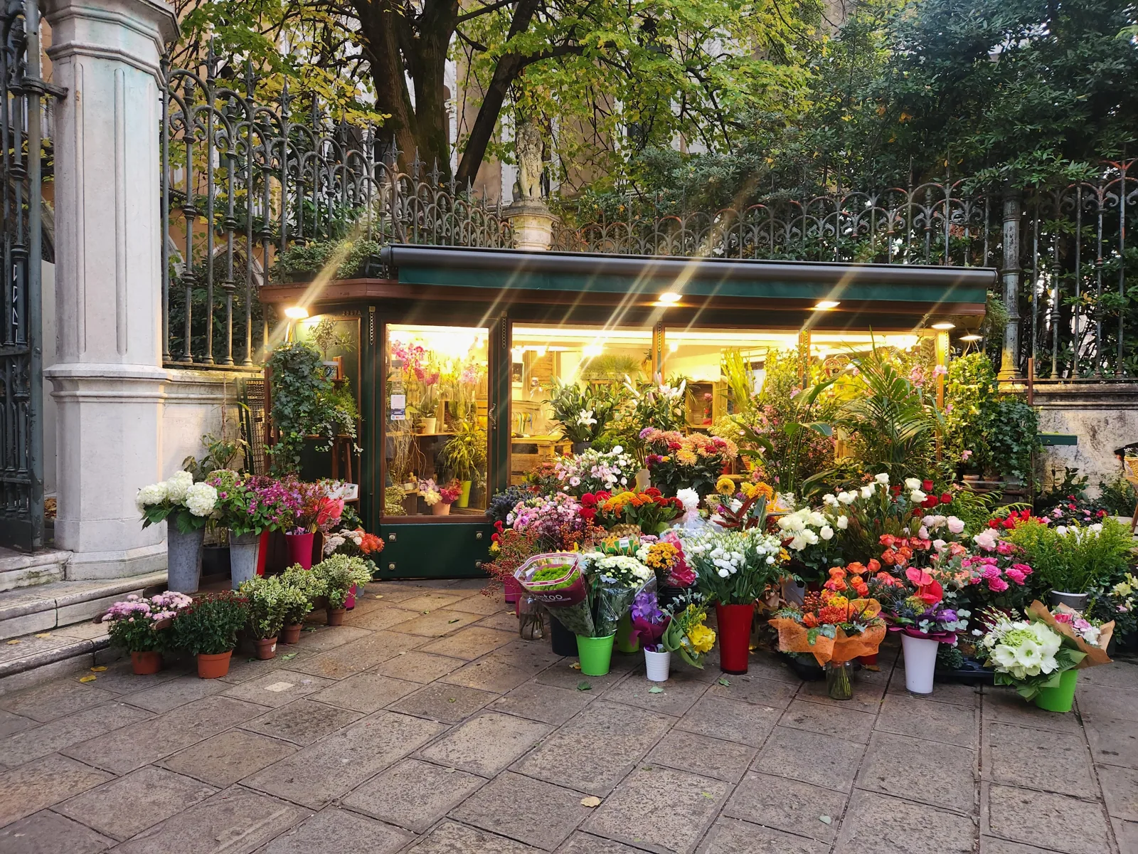 A brightly lit flower stall in a Venice square at dusk