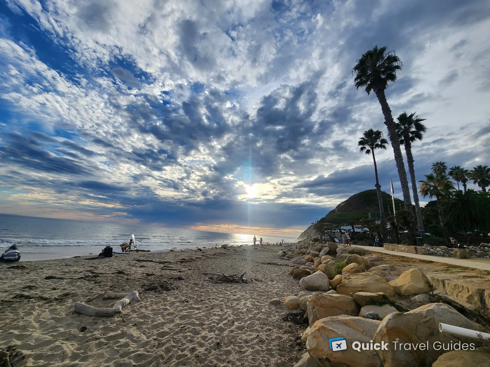 Hendry's Beach in Santa Barbara in the late afternoon, with palm trees, boulders and The Boathouse restaurant under the bluff