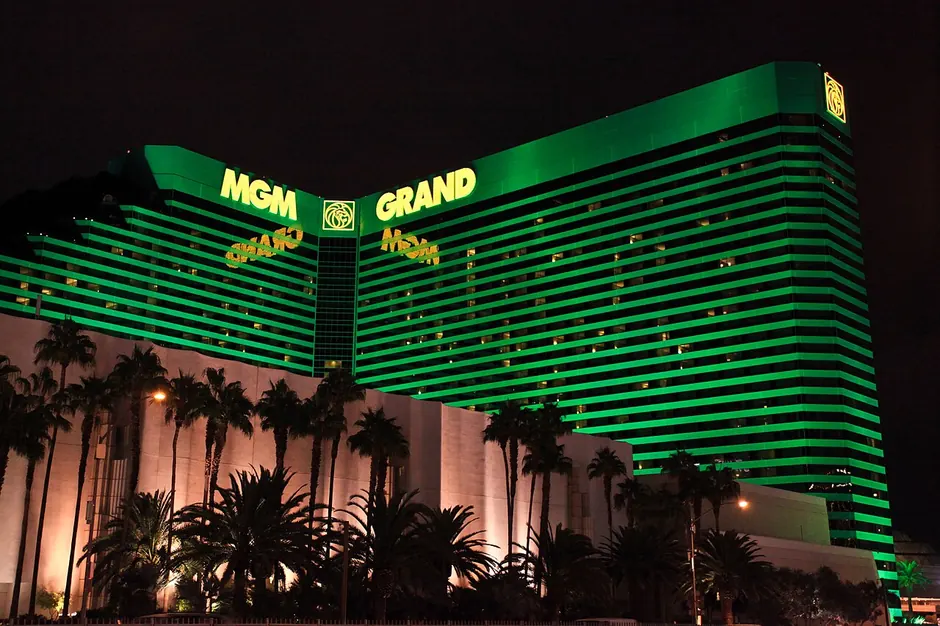 The green towers of the MGM Grand lit up at night behind palm trees
